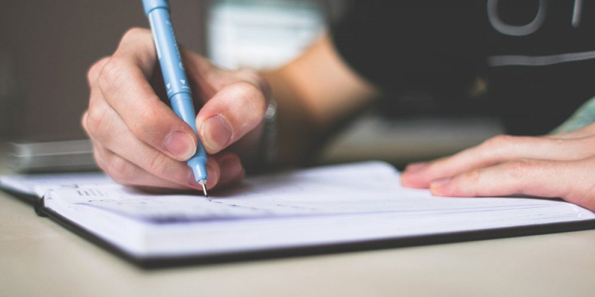 A person holding a pen writing notes in a notebook