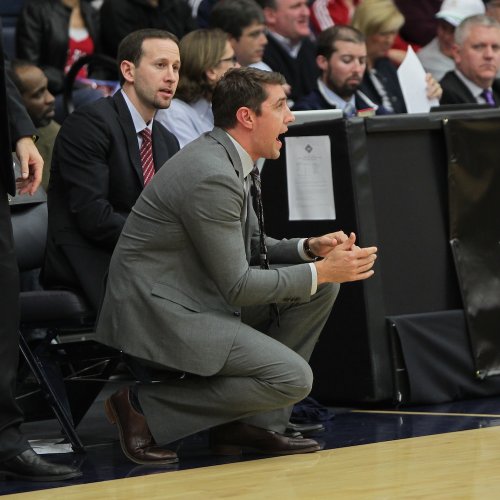 Assistant Coach Adam Caporn kneels at NIT Tournament