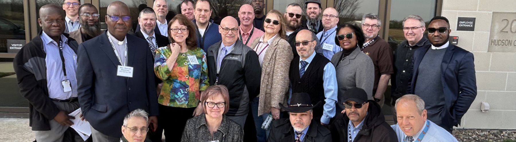 Twenty people in business attire smile for a photo outside a hotel entrance