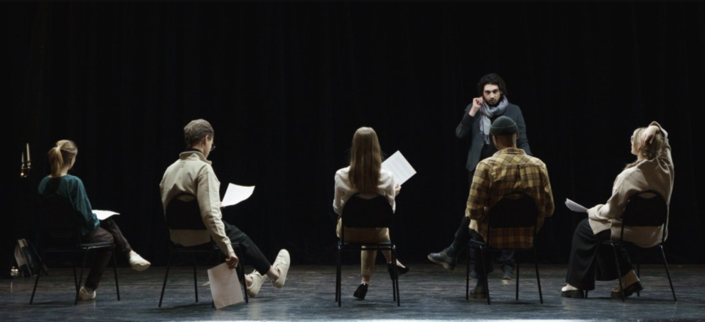 A theatre professor talking to a class of theatre students on stage