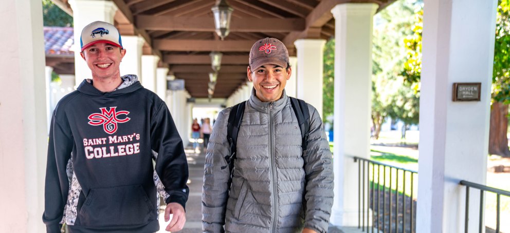 Two students smile at the camera while walking down the outdoor arcade
