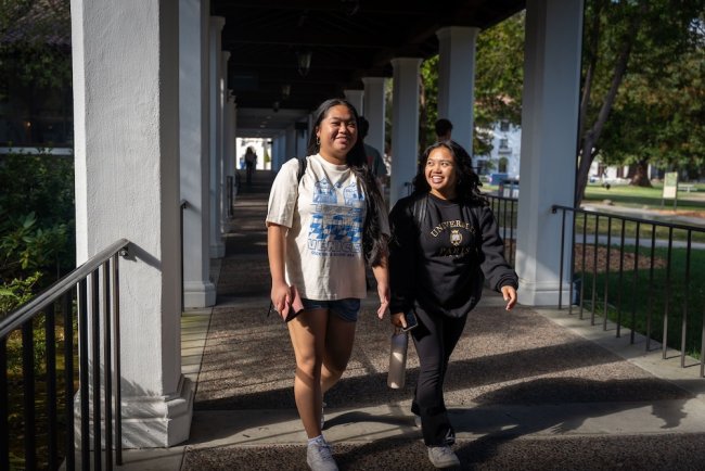 Two students walking beneath the arcade in August 2025