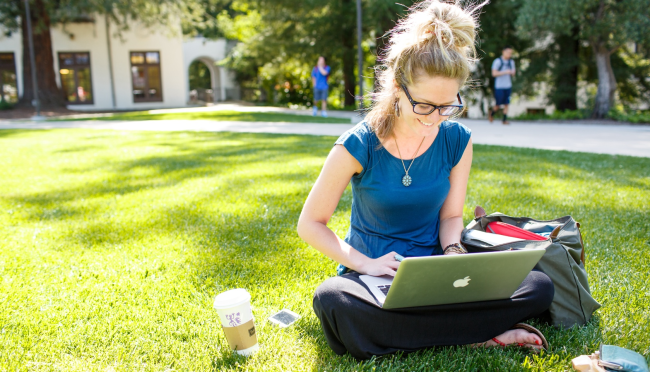 Student with computer sitting in the grass