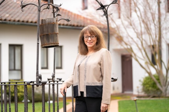 Barbara McGraw standing by well in courtyard in 2026