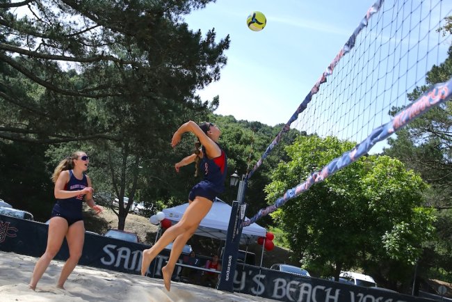 Two Saint Mary's Beach Volleyball players, one jumping to hit the ball