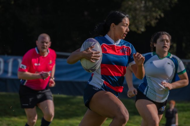 Women's rugby player carries the ball while CSUMB defender chases her