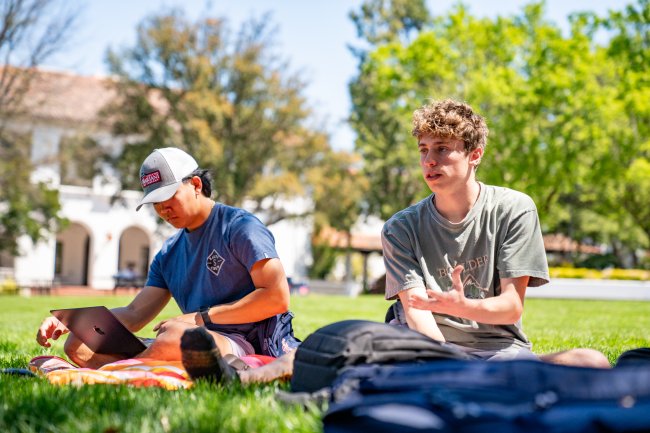 Two male students sitting on lawn for Collegiate Seminar class