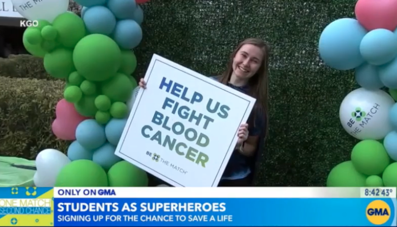 A female Saint Mary's student holds a sign that says "Help Us Fight Blood Cancer"