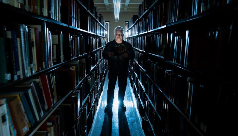 Norm Partidge in library stacks with dramatic lighting, October 2023
