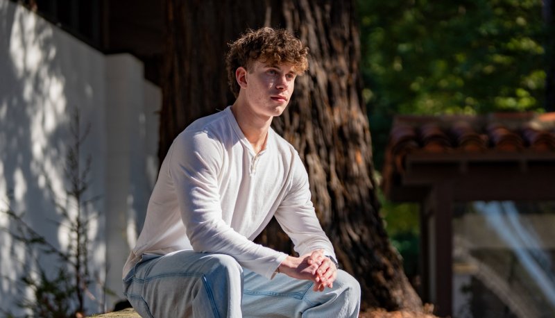 Saint Mary's student Kian Tanner '27 seated on a bench by a redwood