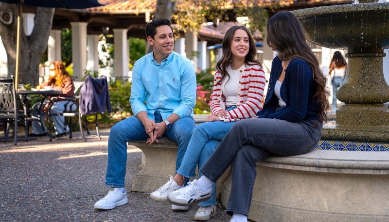 Three students sitting and talking by the fountain in front of the 1928 Pub