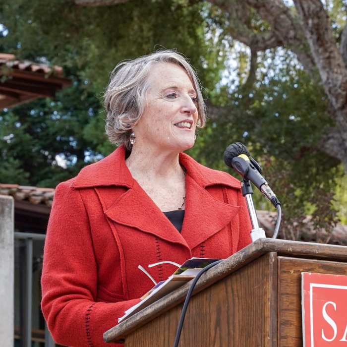 Professor Rosemary Graham in Red jacket speaking at podium outdoors