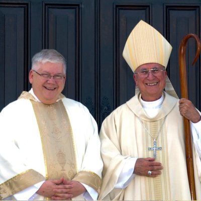 Fr. David Gentry-Akin, left, with Bishop of Stockton. In background is screened-back image of campus.