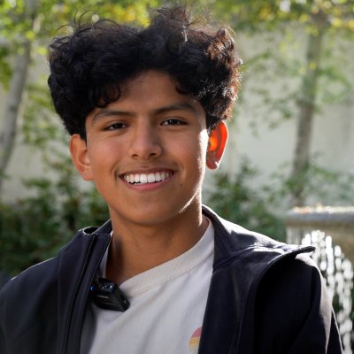 Mitchell Larrieta Angeles smiles at the camera, with a fountain behind him