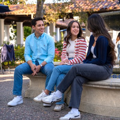 Three students sitting and talking by the fountain in front of the 1928 Pub
