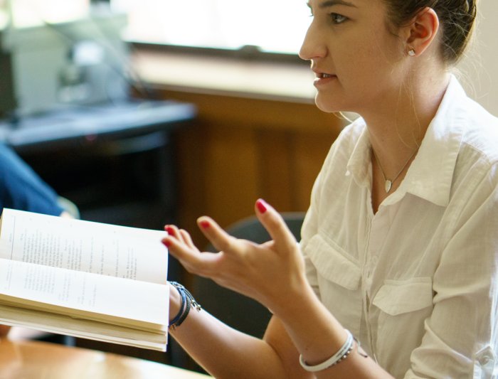 A student gesturing while holding a book in class