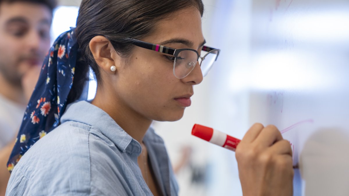 A student is standing up, writing on a whiteboard 